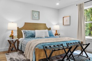 Une chambre à coucher bien rangée, avec un lit en bois, deux tables de chevet avec des lampes, une fenêtre avec des rideaux et une vue sur la verdure à l’extérieur.