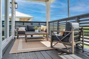 A covered outdoor seating area with a sofa, a chair, and a small table, featuring a view of the sky and greenery. - Preserve Views | Game Room | Direct Beach Access (Saint Augustine)