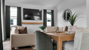 Un salon moderne comprenant un coin repas, un téléviseur à écran plat fixé au mur et une plante en pot.