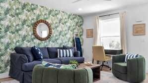 A modern living room with a dark blue sofa, green armchairs, a wooden coffee table, and a ceiling fan.