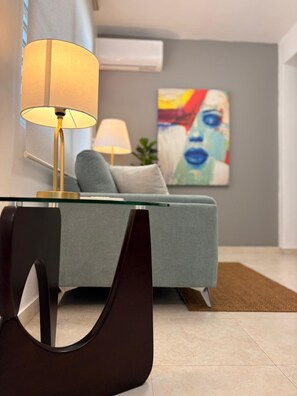 Ein modernes Wohnzimmer mit einem Glastisch, einer Couch, einer Lampe und einem Gemälde an der Wand.