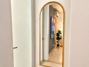 A hallway with a large mirror, a potted plant, and a painting on the wall.