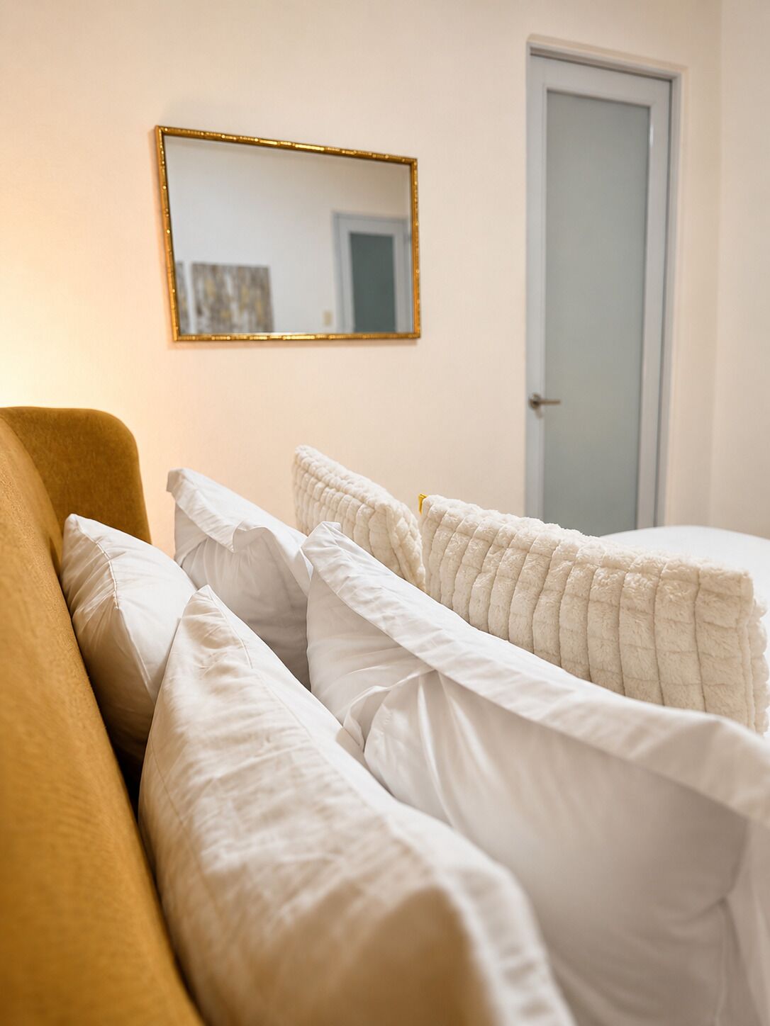 A bedroom with a bed, a sofa, a door, and a mirror on the wall.
