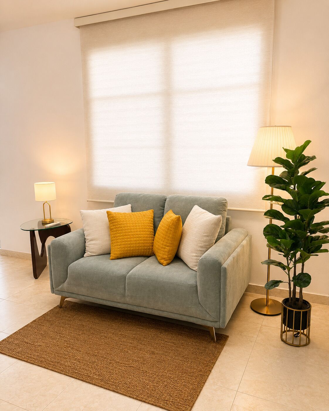 Un salon avec un canapé gris, un tapis marron, une petite table d’appoint avec une lampe et une plante en pot.