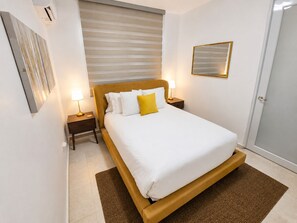 Une chambre à coucher avec un lit, des tables de chevet, un miroir fixé au mur et une porte.