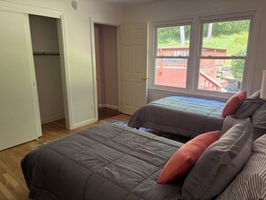 A bedroom with two beds, a closet, and a window with a view of a wooden deck.