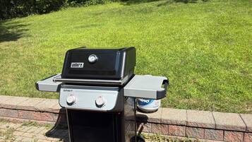 A Weber Spirit portable grill with a side burner, placed on a brick ledge.