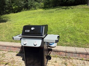 A Weber Spirit portable grill with a side burner, placed on a brick ledge.