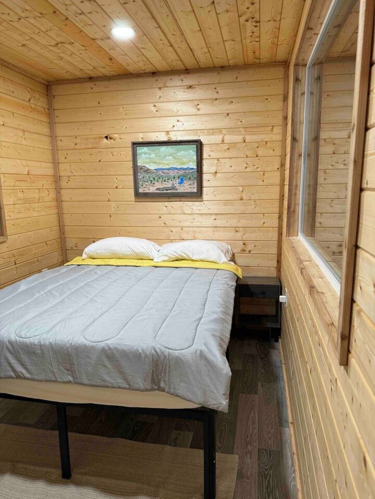 Une pièce de style cabane en bois, avec un lit, un tableau encadré au mur et une fenêtre.