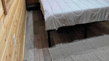 Een kleine houten kamer met een bed, een raam en een nachtkastje.