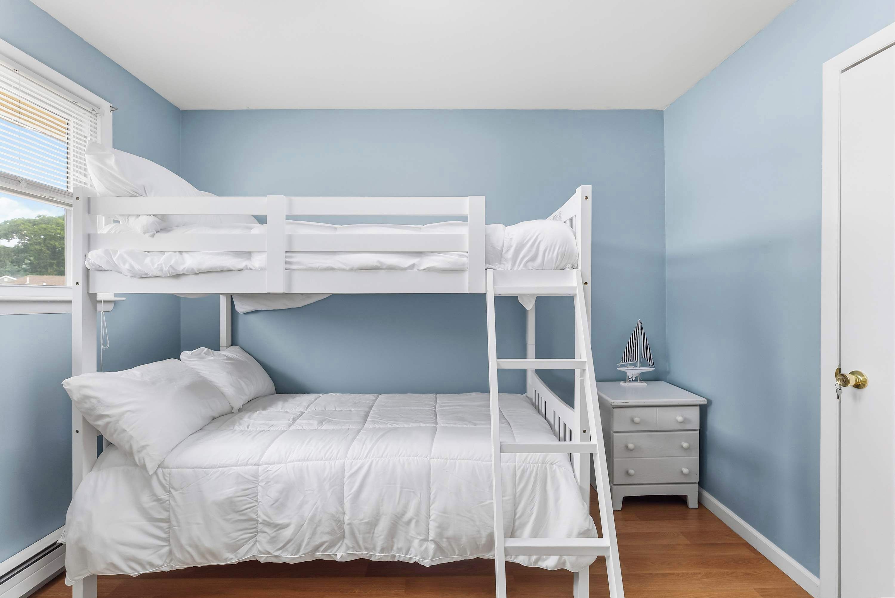 A bunk bed in a room with light blue walls, a small bedside table with a lamp, and a door with a key lock.