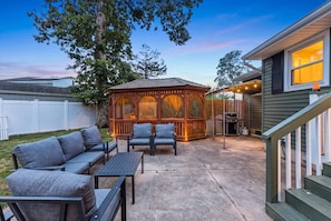 A patio with outdoor furniture, a wooden gazebo, and a house with a visible staircase. - Cape May Escape • Sleeps 10 • Tiki Bar • Grill (Cape May)