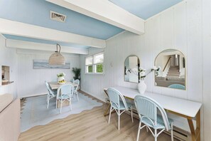 A room with a dining table and chairs, a large mirror, and a ceiling vent. - Cape May Escape • Sleeps 10 • Tiki Bar • Grill (Cape May)