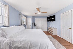 Une chambre à coucher avec un lit, un ventilateur de plafond, une télévision, une armoire et une porte.