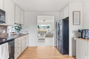 A modern kitchen with white cabinetry, a stainless steel refrigerator, and a coffee maker on the counter. - Cape May Escape • Sleeps 10 • Tiki Bar • Grill (Cape May)