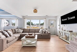 A living room with a sectional sofa, a coffee table, and a television on the wall. - Cape May Escape • Sleeps 10 • Tiki Bar • Grill (Cape May)