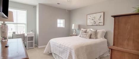 A bedroom with a bed, a desk, a chair, a ceiling fan, and a window.