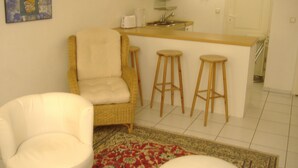 A living room with a white armchair, a wicker chair, and a small bar area with stools. - Hamburg: 3-room apartment, 50 square meters, 3 beds, lodging, vacation rental—including LAST-MINUTE deals (Hamburg)