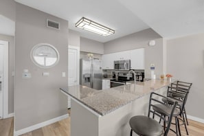 A modern kitchen with a central island, stainless steel appliances, and a dining area with bar stools. - 2-Bedroom Beachfront Condo at Shores of Panama! (Panama City Beach)