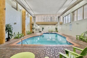 An indoor swimming pool with a tiled floor, surrounded by green chairs and potted plants. - 2-Bedroom Beachfront Condo at Shores of Panama! (Panama City Beach)
