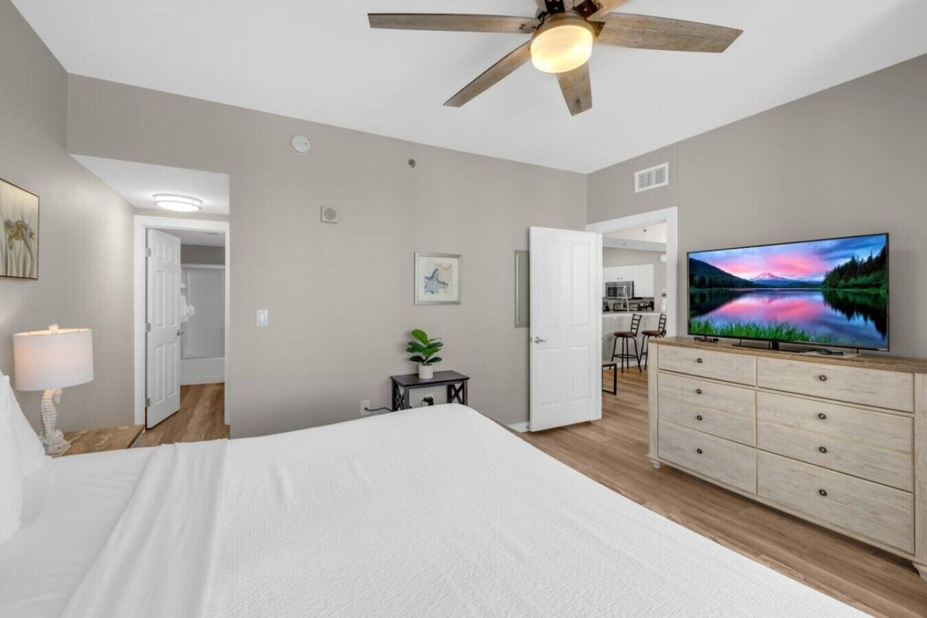 Ein Schlafzimmer mit einem Bett, einem Fernseher, einem Deckenventilator und Blick zur Küche.