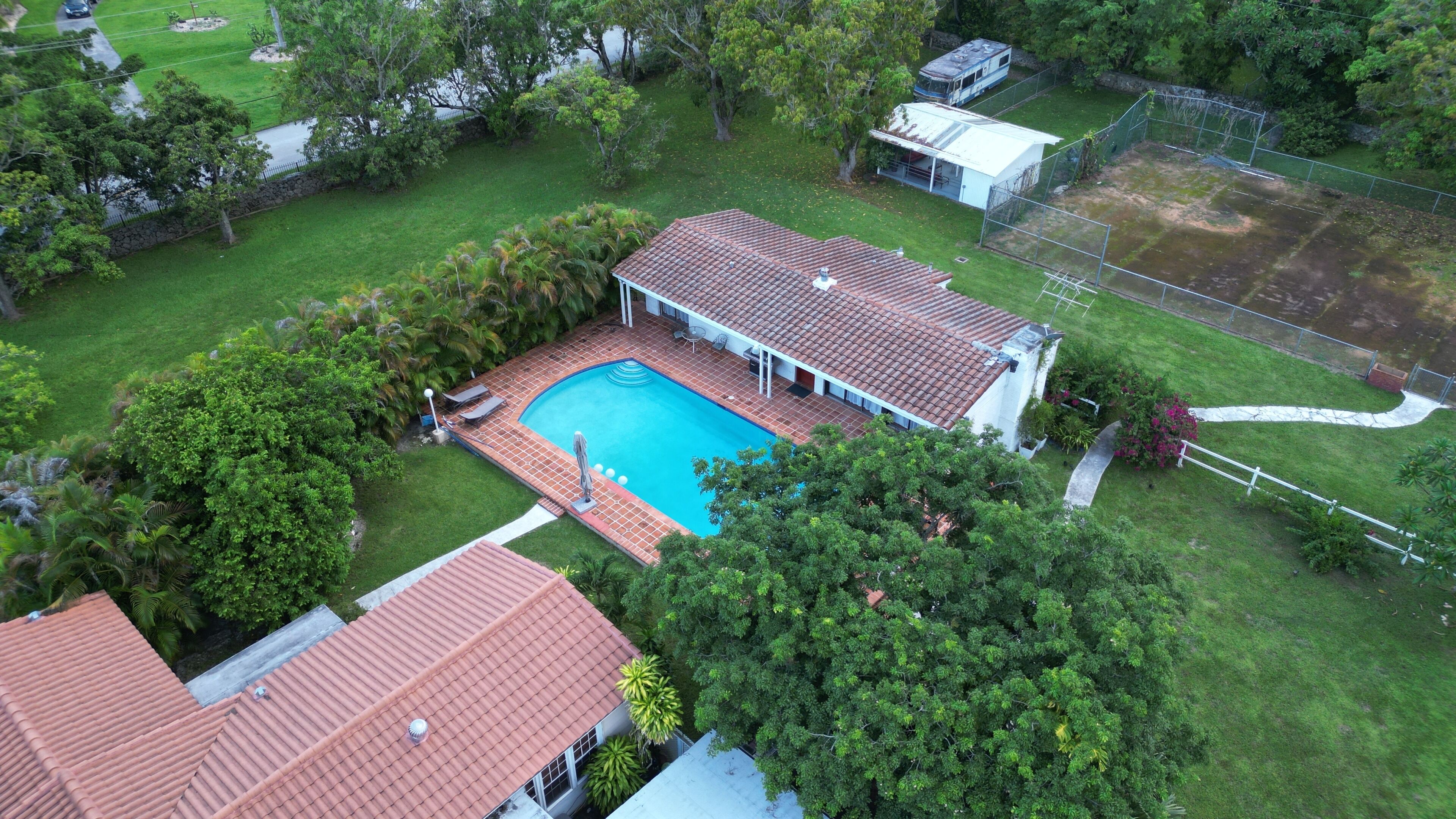 A residential property with a swimming pool, a fenced yard, and a house with a red-tiled roof.