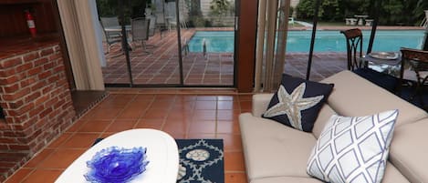 Un salon avec un canapé, une porte vitrée donnant sur une piscine et une cheminée en briques.