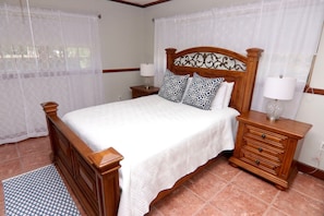 A neatly made bed with a wooden headboard, two bedside tables with lamps, and a patterned rug. - Historic Pool House on 4-acre Mango Farm in heart of Miami-Reduced this Summer (Miami)