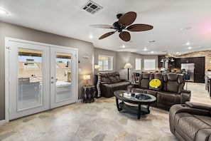 Ein geräumiger Wohnbereich mit Deckenventilator, einer Couch, einem Couchtisch und einer Küche im Hintergrund.