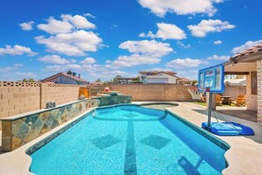 Ein Schwimmbecken mit einem Basketballkorb, umgeben von einer Ziegelmauer und einem strahlend blauen Himmel.