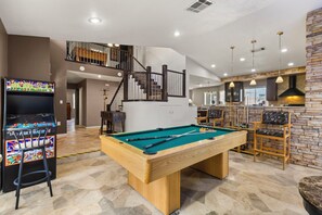 Ein Billardtisch in einem geräumigen Raum mit Treppe, einer Bar und einem Billardbereich.