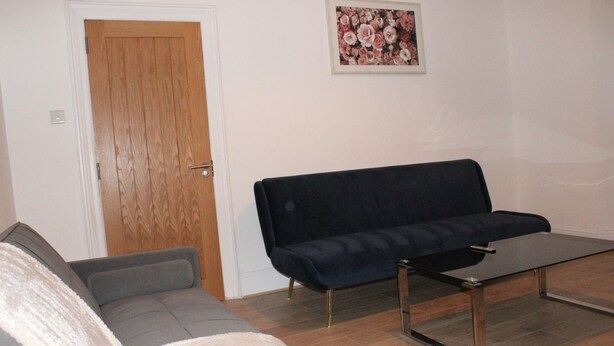 A living room with a grey sofa, a dark blue sofa, and a glass coffee table. - Stylish Bradford Home | Near City Centre | Sleeps 11 (Bradford)