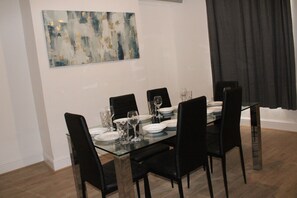 A dining area with a glass table, black chairs, and white plates. - Stylish Bradford Home | Near City Centre | Sleeps 11 (Bradford)