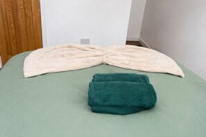A bed with a green sheet and two folded blankets, one beige and one teal. - Contractors or Families | Sleeps 12 + Fast WiFi | Near Bradford University + BRI (Bradford)