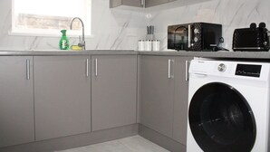 A kitchen with grey cabinets, a washing machine, a microwave, and a window with a view. - Stylish Bradford Home | Near City Centre | Sleeps 11 (Bradford)