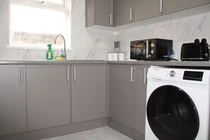 A kitchen with grey cabinets, a washing machine, a microwave, and a window with a view. - Stylish Bradford Home | Near City Centre | Sleeps 11 (Bradford)