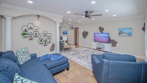 A living room with a sofa, a television, and a decorative wall. - Heated Pool & Spa • 3 BRs • 10 min to Siesta Key (Sarasota)