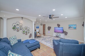 A living room with a sofa, a television, and a decorative wall. - Heated Pool & Spa • 3 BRs • 10 min to Siesta Key (Sarasota)