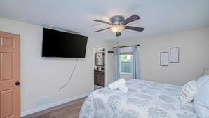 A bedroom with a bed, a ceiling fan, a television, and a door. - Heated Pool & Spa • 3 BRs • 10 min to Siesta Key (Sarasota)