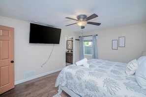 A bedroom with a bed, a ceiling fan, a television, and a door. - Heated Pool & Spa • 3 BRs • 10 min to Siesta Key (Sarasota)