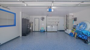A laundry room with a ceiling-mounted projector, a large fan, and a small cooler. - Heated Pool & Spa • 3 BRs • 10 min to Siesta Key (Sarasota)