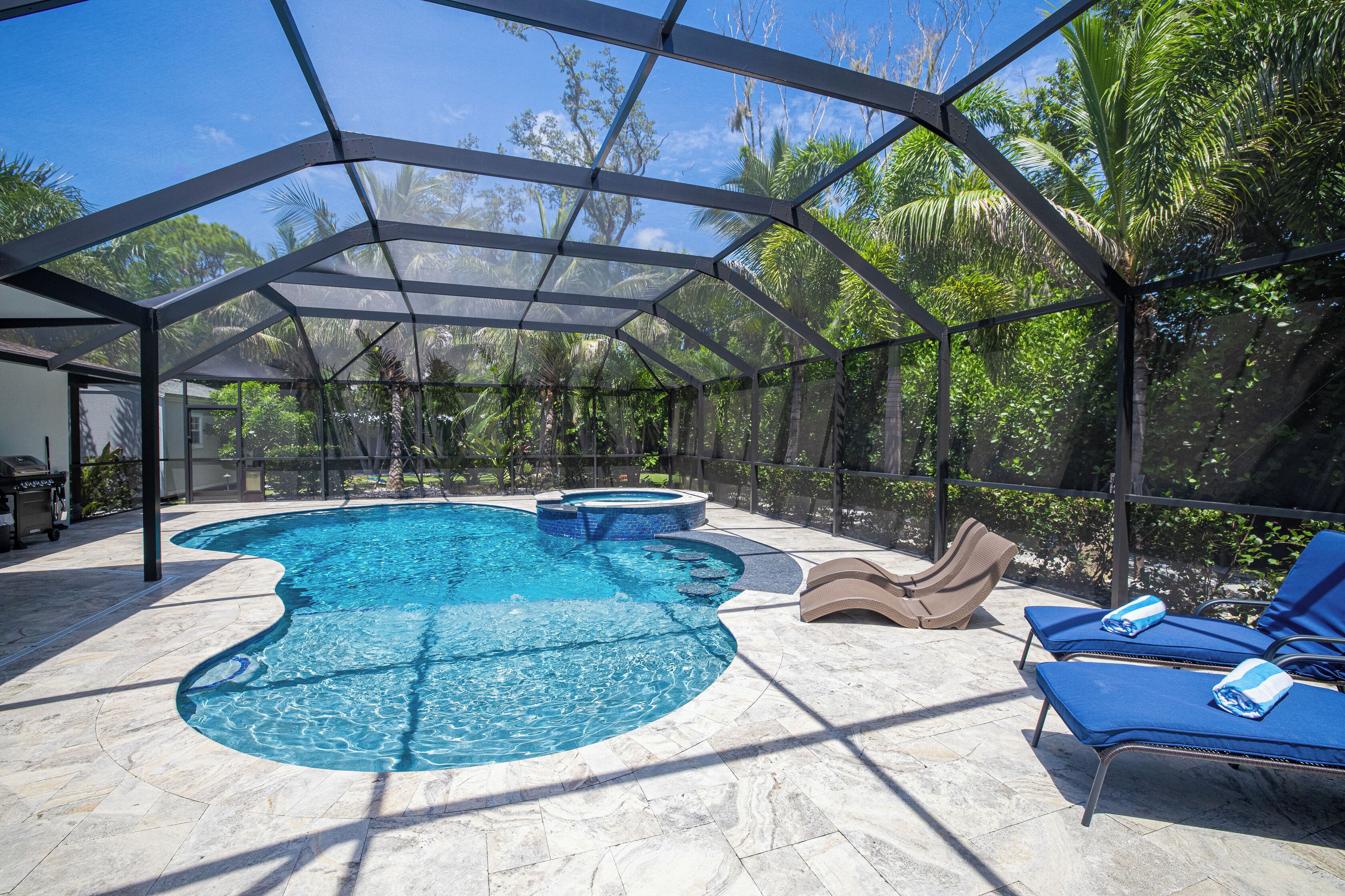 A covered outdoor swimming pool with lounge chairs and a barbecue area.