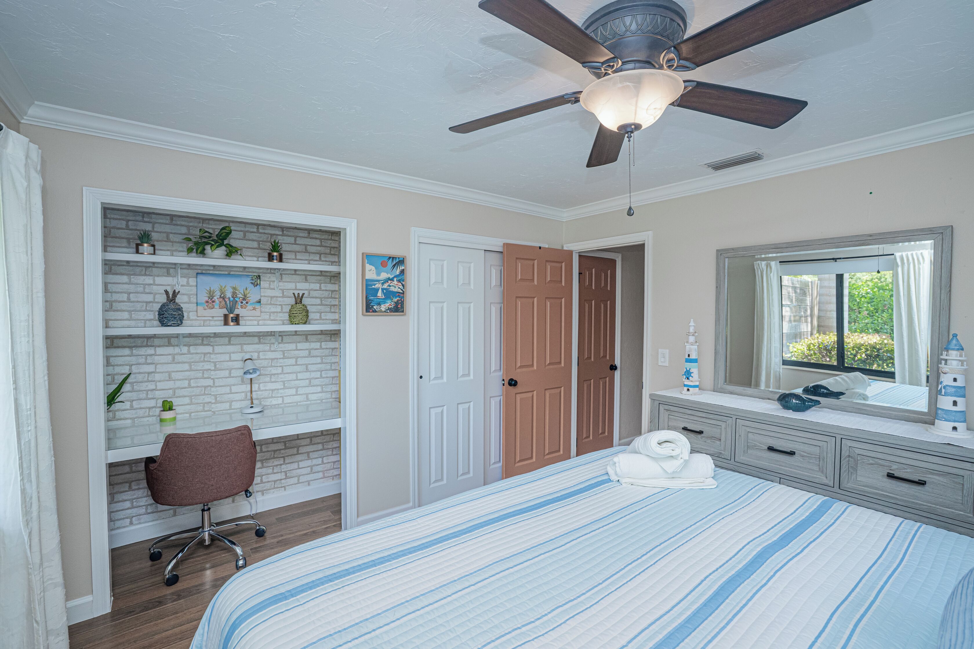 A bedroom with a bed, a desk, a chair, a wardrobe, and a ceiling fan.