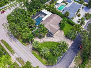 An aerial view of a residential area with a swimming pool, a covered patio, and lush greenery. - Heated Pool & Spa • 3 BRs • 10 min to Siesta Key (Sarasota)