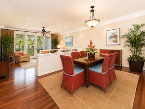 A spacious living area with a dining table, red upholstered chairs, a ceiling fan, and a view of the outdoors through large windows.