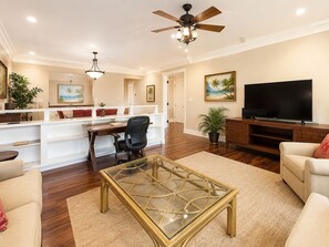 Ein geräumiges Wohnzimmer mit einem Glastisch, einer Couch, einem Fernseher und einem Deckenventilator.
