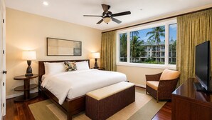A hotel room with a large bed, a sitting area with a chair, a television, and a view of palm trees through the window. - Beachfront 6BR, 2 Condos for 16 at Turtle Bay! (Kahuku)