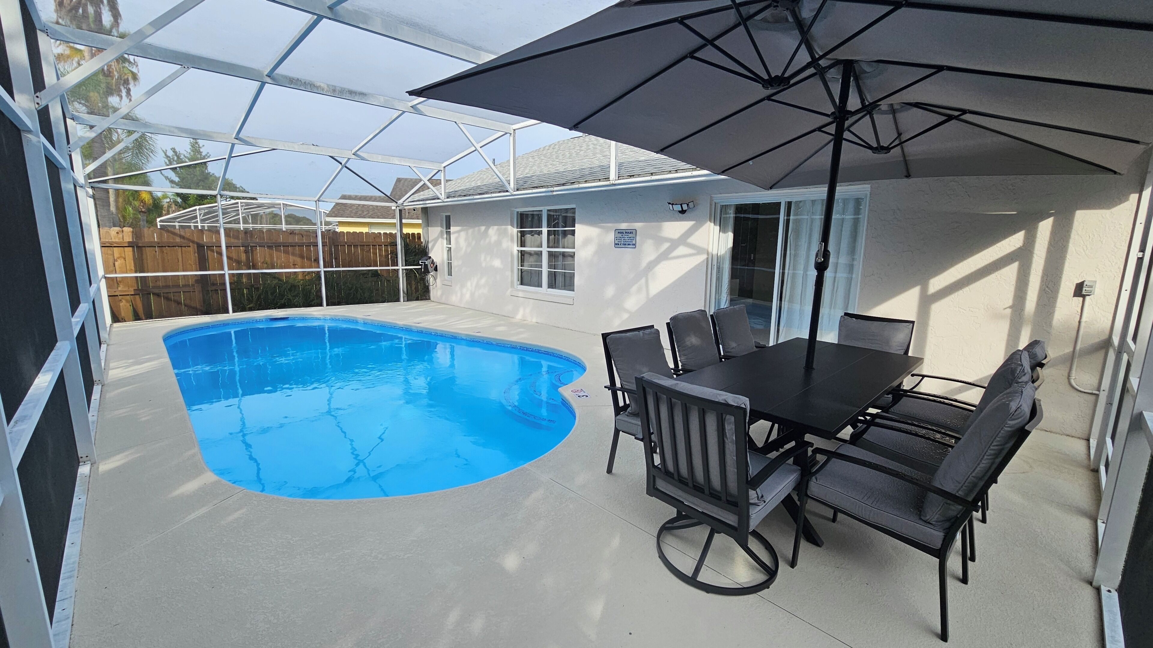 A covered outdoor area with a pool, a table with chairs, and a patio umbrella.