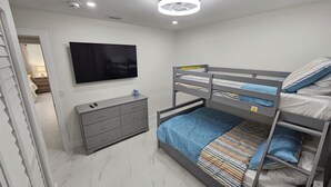 Une chambre avec un lit superposé, un téléviseur à écran plat fixé au mur, une commode grise et un sol en marbre.