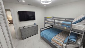 A bedroom with a bunk bed, a flat-screen TV mounted on the wall, a grey dresser, and a marble floor.